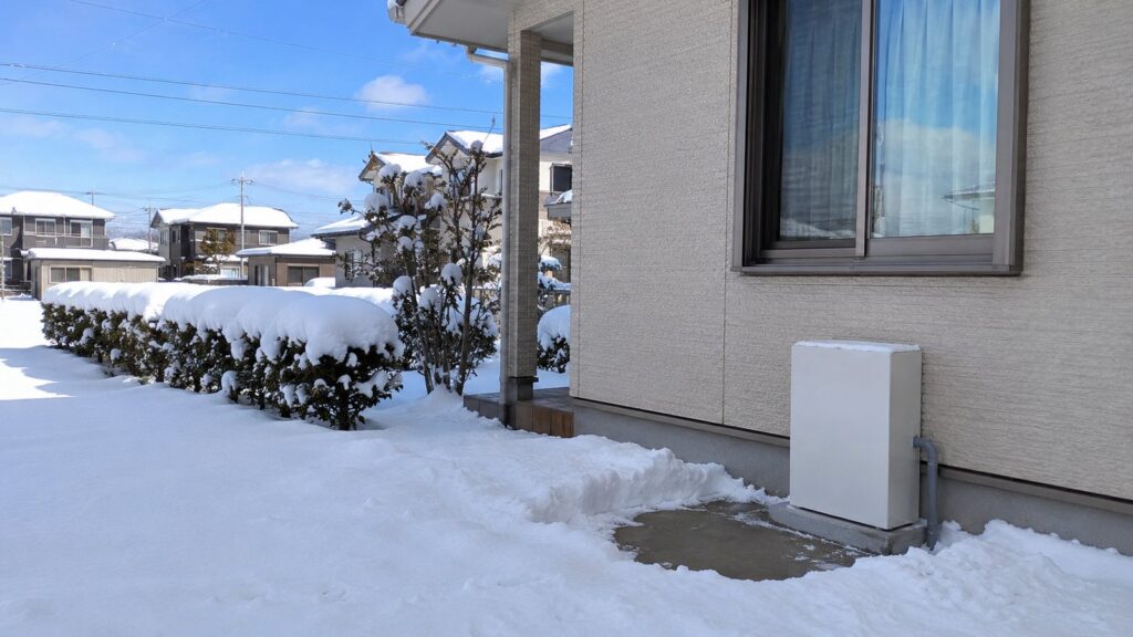 雪が積もった住宅の外壁沿いに設置された家庭用蓄電池のユニット。周囲だけ雪かきされている