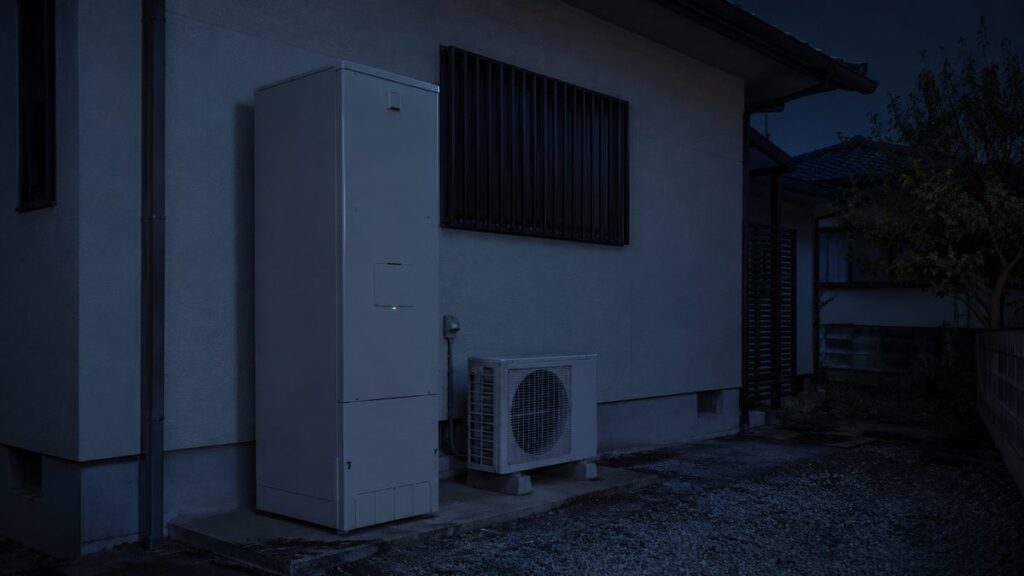 深夜の戸建て住宅の外壁ぎわに設置されたエコキュートの貯湯タンクとヒートポンプユニット