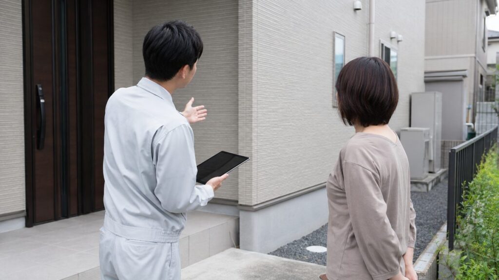 住宅の玄関先で、施工会社のスタッフが住人に蓄電池の設置場所を説明している様子