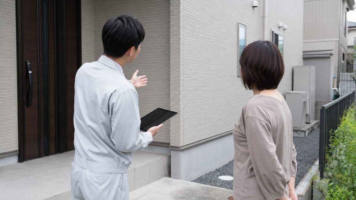 住宅の玄関先で、施工会社のスタッフが住人に説明している様子